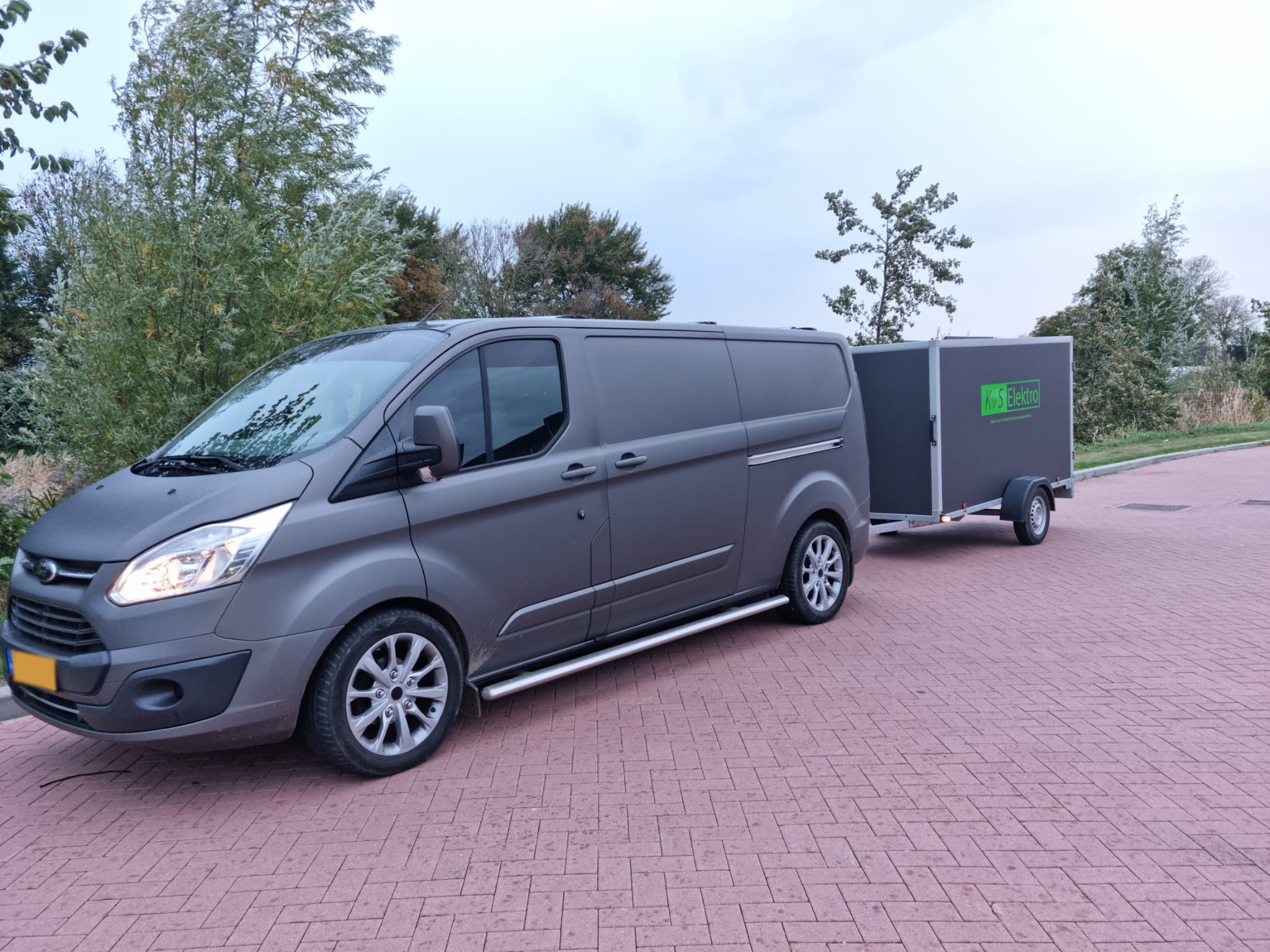 Bedrijfsbus van KvS Elektro met de aanhanger erachter